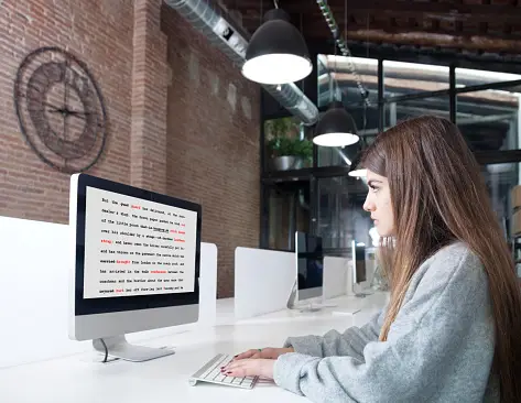 A woman reading a document on a computer screen checking errors in red font