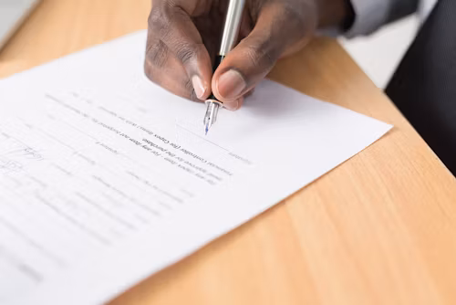 A man's hands signing a paper on a desk