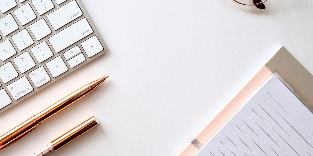 A keyboard, a pen, and a pad of paper on a desk