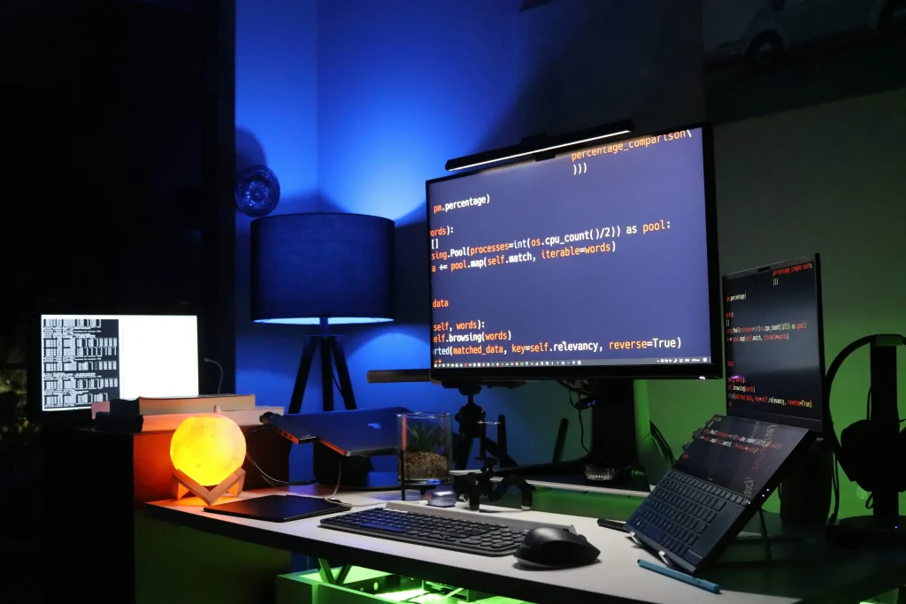 A vibrant desk with multiple screens displaying code, reflecting a programming or software development workspace.