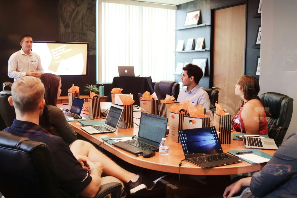 A corporate meeting or workshop with participants seated around a table, engaging with a presenter and discussing ideas.