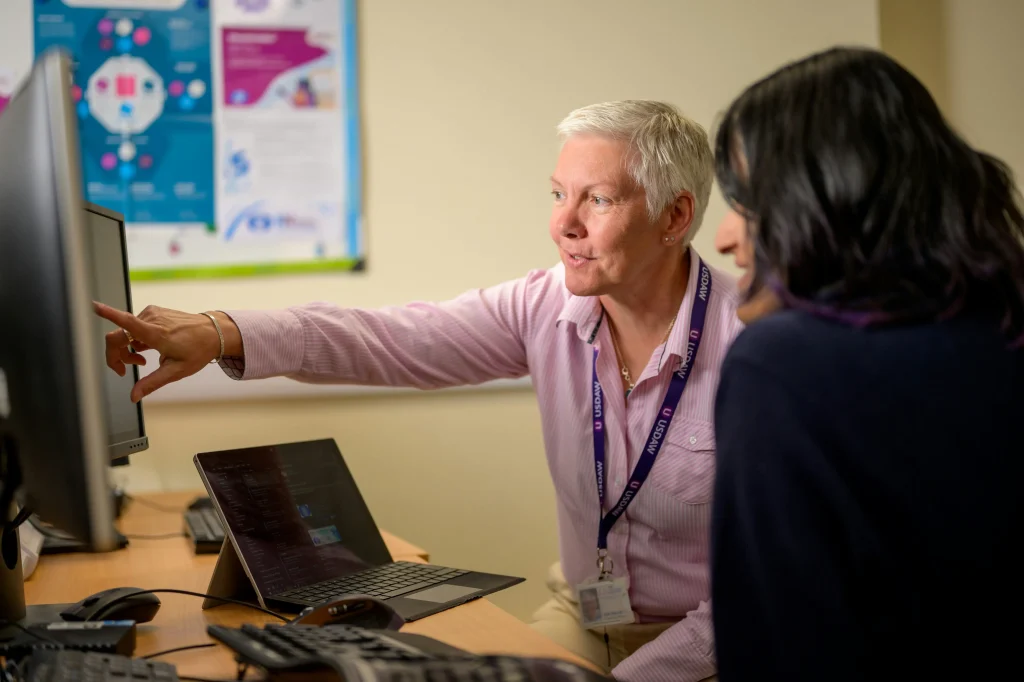 A professional guiding another person on a computer, showcasing mentorship or collaboration in a professional setting.