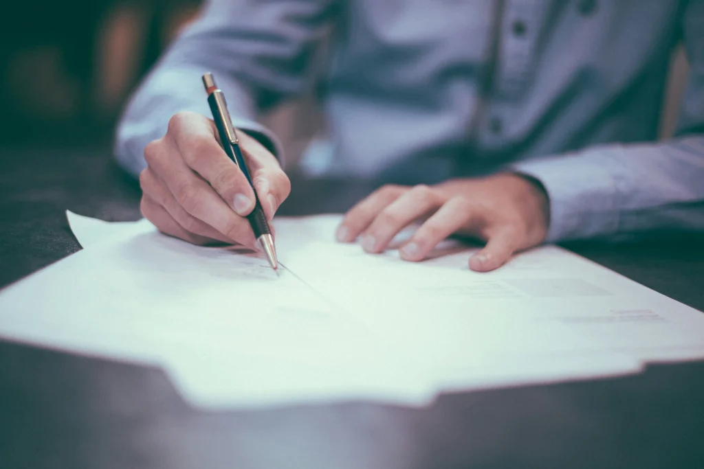 A person writing on a document, signifying paperwork, contracts, or legal documentation.